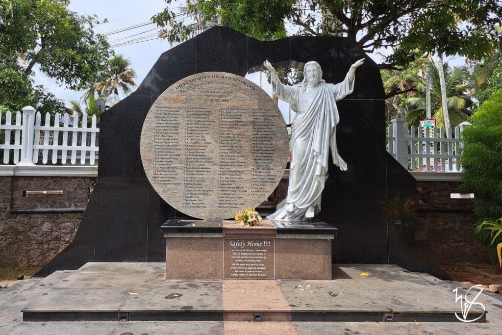 A stone memorial located outside the church, where the resurrected Christ has his arms outstretched toward Heaven, standing beside a circular monument containing all the names of the deceased. Flowers have been left here, and an inscription below reads as follows,

Safely Home
I am home in Heaven, dear ones;
Oh, so happy and so bright.
There is perfect joy and beauty
in this everlasting light.
All the pain and grief is over,
Every restless tossing passed,
I am now at peace forever,
Safely Home in Heaven at last.